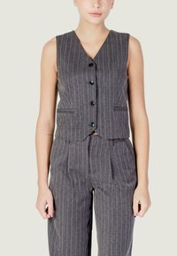 Gilet smanicato grigio a righe con scollo a V, bottoni frontali e tasche laterali, abbinato a pantaloni coordinati con righe verticali.