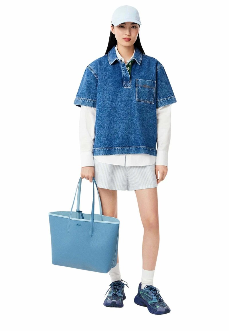 Camicia di jeans oversize, maglia bianca a maniche lunghe, pantaloni corti a righe, borsa a spalla blu e sneakers multicolori, caratterizzate da un design elegante e texture morbide.
