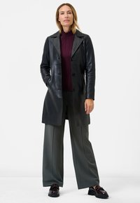 Black leather trench coat with a notched lapel, double-breasted buttons, and side pockets, paired with a ribbed burgundy top and striped pants.
