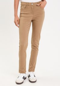 Jean skinny tan en mélange de coton. Comprend des poches avant, une fermeture à bouton et une texture lisse. Associé à des baskets blanches et noires.