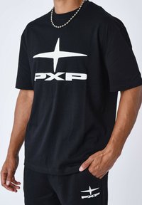 Camiseta de algodón negra con un gráfico blanco que presenta el logo "PXP" y una estrella. Mangas cortas y un ajuste relajado, con una textura suave.