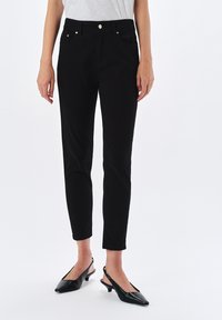Czarne dopasowane spodnie z talią na średnim poziomie, z dwoma przednimi kieszeniami, niewielkimi srebrnymi detalami i gładkim, teksturowanym materiałem.