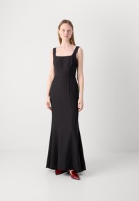 Black floor-length dress with a square neckline and fitted bodice, flaring gently at the hem. Paired with red pointed-toe shoes.