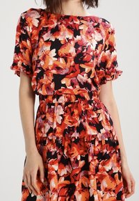Bloemendress met een zwarte basis en levendige rode, oranje en roze bloemen, korte puffmouwen en een geplooide taille.