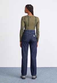 Pantaloni din denim albastru închis cu talie înaltă, dotati cu două buzunare pe spate și un etichetă cu logo. Asortați cu un top lung cu mâneci lungi, de culoare verde măsliniu, cu efect tie-dye.