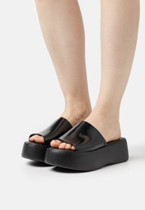 Infradito neri con platform, design aperto e lucido, suole in gomma spesse. Texture liscia, stile minimalista e forma curva.