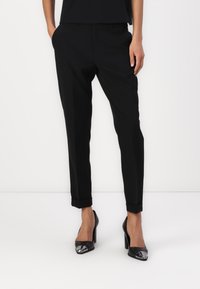 Sorte skreddersydde bukser med slim fit, med flat front, sidelommer og oppbrett, kombinert med sorte høyhælte sko med metalliske spisser.