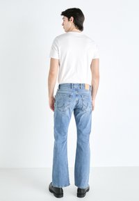 Ljusblå denimjeans med rak ben, som har två bakfickor och en läderlapp på midjan. Bärs med en vit t-shirt.
