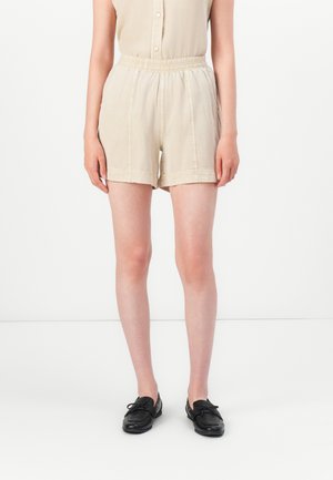 Beige lette shorts med elastisk midje, med sydd detaljer og løs passform. Kombinert med svarte slip-on sko.