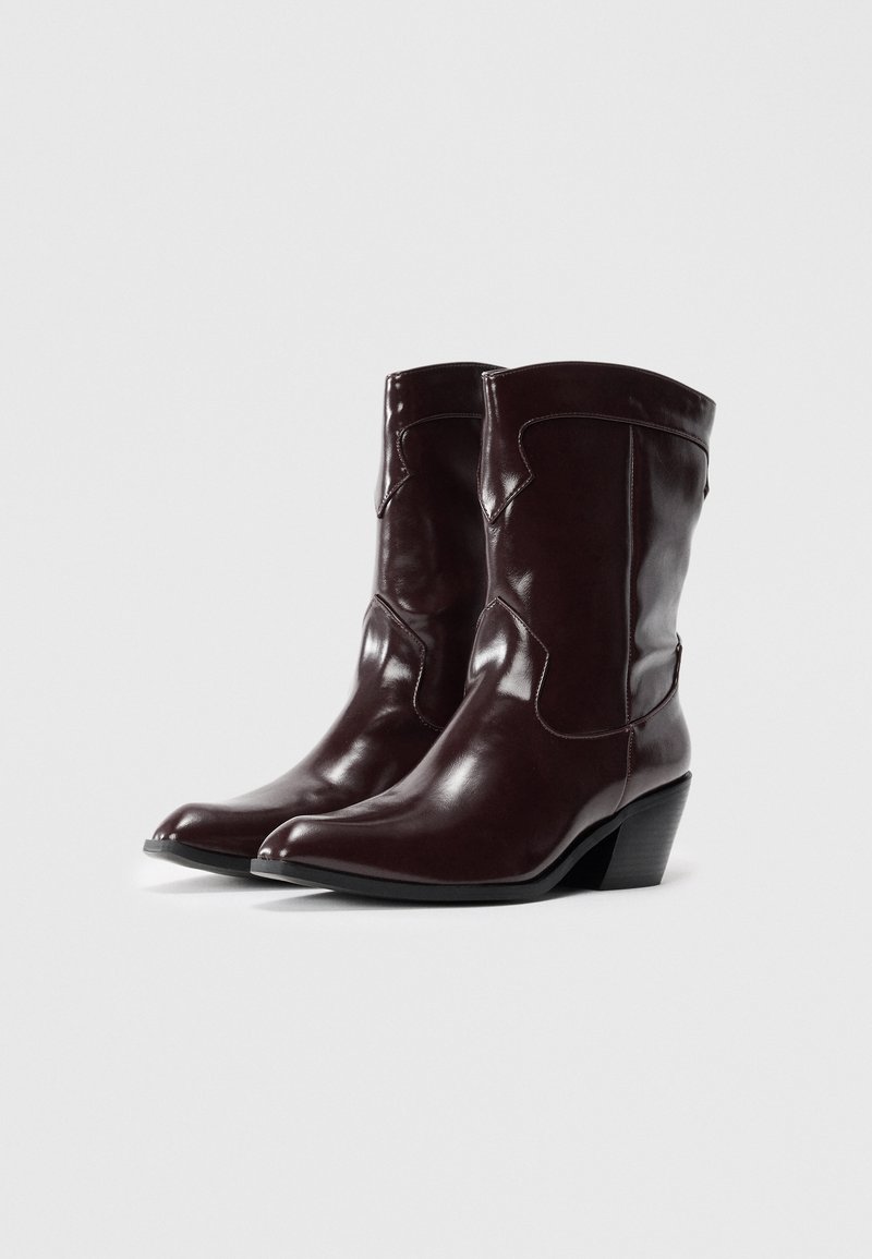 Stivali da cowboy in pelle bordeaux con punta affusolata, cuciture decorative e tacco di altezza media. Texture liscia con una finitura elegante.