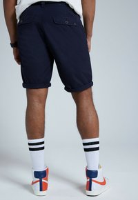 Námořnické modré šortky s ohrnutými manžetami, zadní kapsy s knoflíky. Nosené s bílými ponožkami po kolena a vícebarevnými sneakers na vysoké podrážce.
