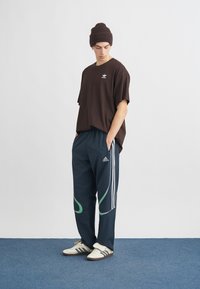 Ruda, per didelį dydį tinka marškinėliai, tamsiai mėlyni kelnės su žaliais akcentais, trys baltos juostelės ir marginti balti sportbačiai. Modelis dėvi rudą megztinį beanie.