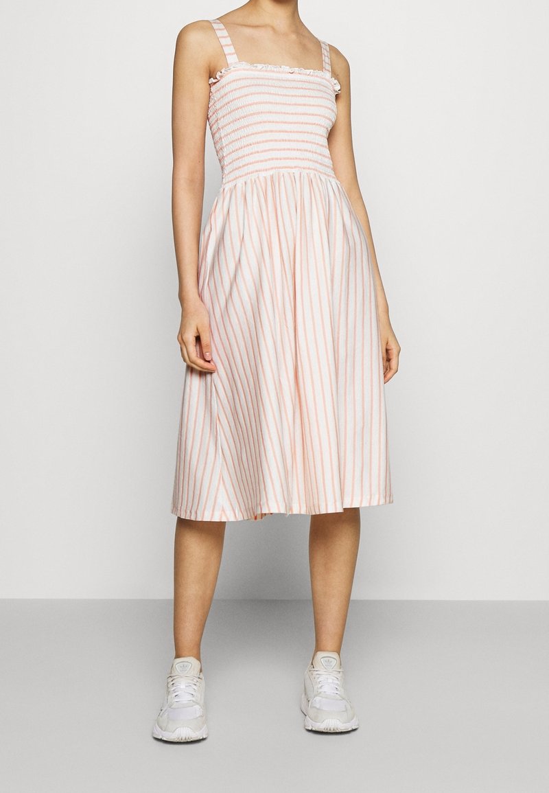 Lättviktig ärmlös klänning med horisontella och vertikala ränder i ljusrosa och vitt, med en smockad liv och utsvängd kjol.