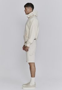 Lichtbeige hoodie met een hoge hals, een voorzak, gecombineerd met bijpassende shorts. Geweven schoenen en witte sokken maken de look compleet.