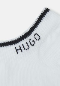 Fehér zokni fekete "HUGO" logóval. Simá szövetű, és kontrasztos varrás található a felső szélén. Egyszerű és minimalista dizájn.
