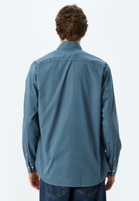 Camisa de manga larga en azul desgastado, de tela de algodón. Presenta un cuello, puños con botón y un dobladillo curvado para un ajuste relajado.