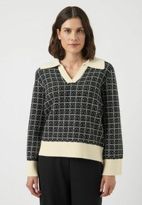 Svart och krämfärgad stickad tröja med V-ringning, kontrasterandekrage, rutigt mönster samt ribbade muddar och fåll. Lös passform.