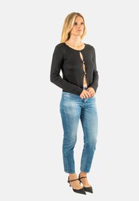 Cardigan nero a coste con scollo rotondo e chiusura a bottoni. Abbinato a jeans azzurri chiari e décolleté nere a punta.