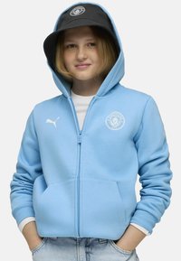 Svetlomodrá mikina na zips s klokankovými vreckami, s bielym logom Puma a emblémom Manchester City na ľavej strane hrudi. Bavlnený materiál.