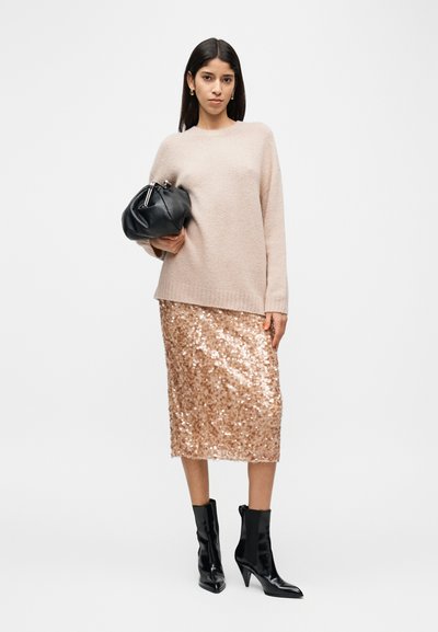 Ροζ ανοιχτό ροζ πλεκτό πουλόβερ, μίντι φούστα σε ροζ χρυσό με παγιέτες, μαύρη τσάντα χειρός και γυαλιστερά μαύρα μποτάκια μέχρι τον αστράγαλο, παρουσιάζοντας μια μοντέρνα και υφασματική εμφάνιση.