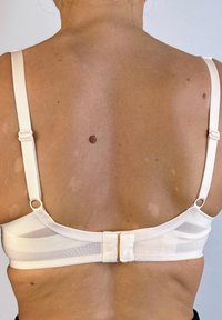 Sostén de color beige claro con tirantes ajustables, diseño de malla y un cierre central. Textura suave con detalles de costura mínimos.