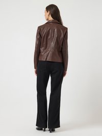 Giacca aderente in pelle marrone con colletto a rever, vista da dietro. Sono visibili anche un paio di pantaloni neri svasati e scarpe con tacco.