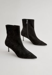 Black suede ankle boots with pointed toes, zip closure on the side, and thin stiletto heels. Smooth texture and fitted design.