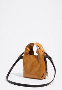 Skórzana torebka w kolorze brązowym o sztywnym kształcie, z gładką teksturą, unikalnym wycięciem na uchwyt oraz regulowanym, ciemnobrązowym paskiem na ramię. Posiada boczną kieszeń.