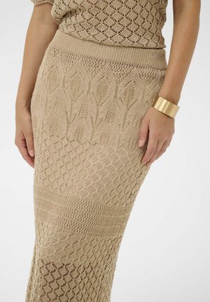 Beige színű kötött maxi szoknya mintás textúrákkal, gyémánt és levél formákkal díszítve. Arany mandzsetta karkötővel a csuklón.