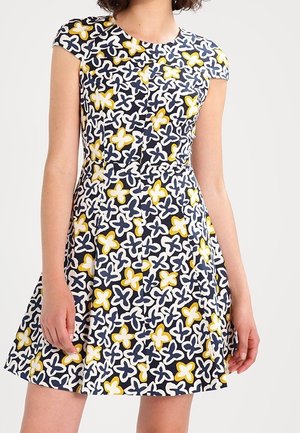 Femme portant une robe à manches courtes, longueur genou, avec une taille cintrée et un motif floral abstrait bleu marine, blanc et jaune.