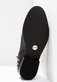 Stivale in pelle nera con texture liscia, decorazioni a borchie sui lati e suola in gomma con logo vicino al tallone.