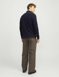 Mörkblå stickad tröja med hög krage och raglanärmar, tillsammans med bruna vida byxor. Outfiten har en avslappnad passform och en mjuk textur.