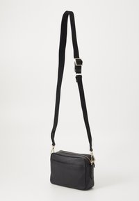 Borsa a tracolla in pelle nera con forma rettangolare, cinturino regolabile, accessori in oro e chiusura con zip. Presenta una tasca frontale.
