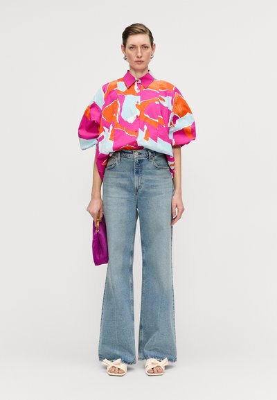 Colorful short-sleeve button-up shirt in pink, orange, and light blue patterns, paired with high-waisted flared denim jeans and white sandals.