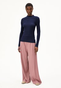 Dunkelblauer gerippter Rollkragenpullover mit langen Ärmeln, kombiniert mit lockeren, hellrosa weit geschnittenen Hosen und beigen Slippern.