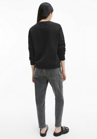 Sudadera negra con cuello redondo, jeans de mezclilla grises y sandalias negras. El atuendo presenta detalles mínimos y un ajuste relajado.