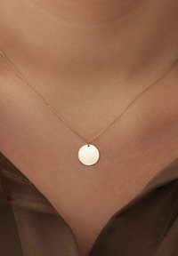 Collier en pendentif en or avec un disque circulaire lisse sur une chaîne délicate. La chaîne a une texture fine, et le pendentif est poli et réfléchissant.