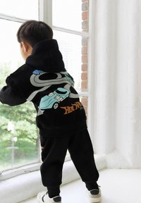 Black hoodie with colorful car graphics and grey winding road design on the back, paired with black jogger pants and white sneakers.