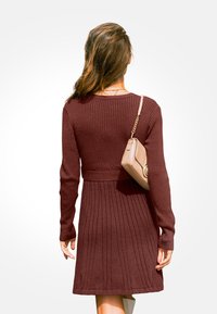 Pruhované vínové svetr šaty s dlouhými rukávy a staženým pasem, doplněné malou béžovou crossbody taškou. Hladká pletená textura.