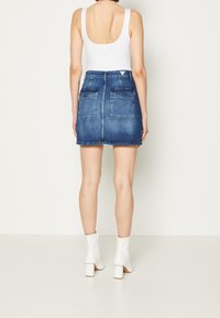 Denim mini kjol i medelblå tvätt med två bakfickor. Kombinerad med en vit åtsittande linne och vita ankelboots med klack.