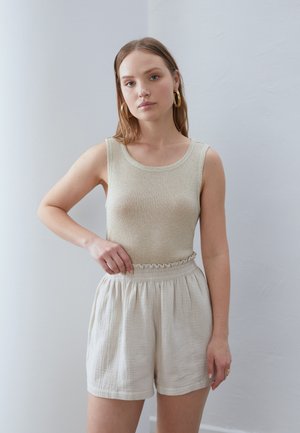 Beige ribbed tank top with rounded neckline paired with light beige, ruffled waist shorts made of textured fabric. Soft, casual look.