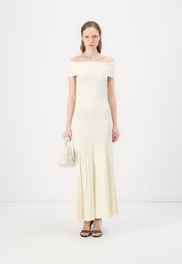 Robe ivoire décolletée, avec un corsage ajusté et une jupe plissée. Associée à un petit sac blanc et des talons noirs à lanières.