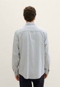 Camisa abotonada de algodón ligero con rayas verticales azules y blancas, mangas largas y un dobladillo curvado. Detalle visible de botón en los puños.