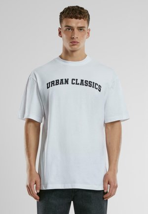 Fehér pamut póló rövid ujjakkal, fekete "URBAN CLASSICS" felirattal a mellkason. Slim fit és kerek nyakú kialakítás.