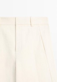 Pantalon taille haute couleur blanc cassé avec passants de ceinture, fermeture avant cachée et poches latérales à l'avant.