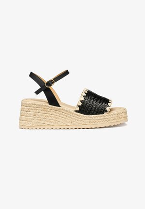 Sandale compensée espadrille avec bride tressée noire sur le bout, bride à boucle noire à la cheville, et semelle plateforme en jute naturel.