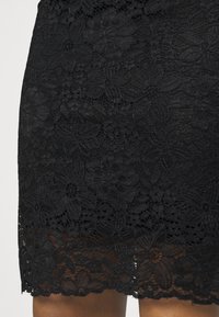 Svart spetskjol med blommönster, scallopkant, texturerad tyg och semitransparent utseende vid nederkanten.