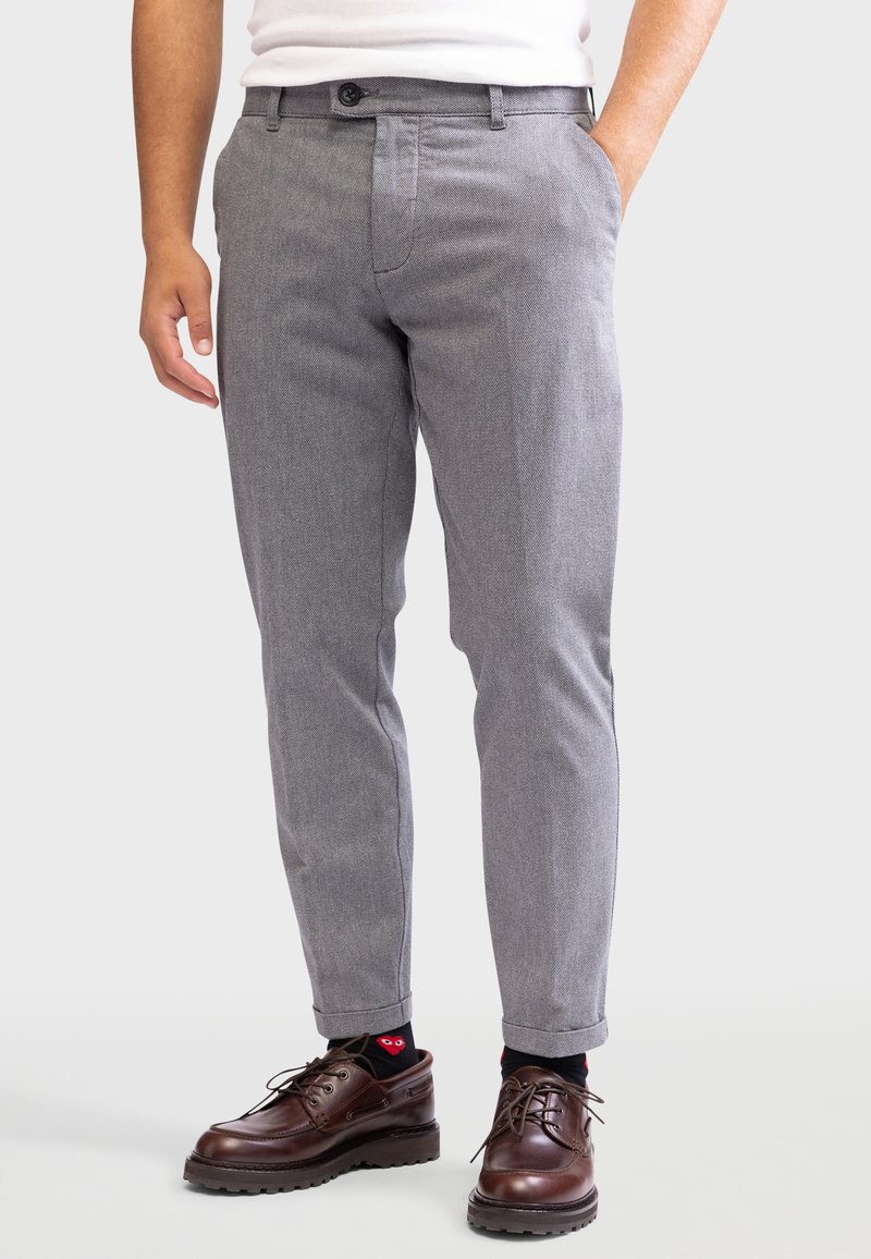 Grijze op maat gemaakte broeken met een textuurafwerking, slim fit, riemlusjes en een ritssluiting. Gepaard met bruine veterschoenen en gestreepte sokken.