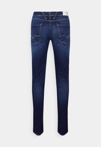Jeans de denim azul oscuro con un corte slim, que cuentan con bolsillos traseros con un sutil detalle de costura y un corte de pierna recta.