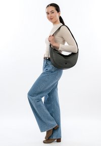 Woman wearing beige textured sweater, high-waisted wide-leg jeans, brown boots, and carrying a large black shoulder bag.